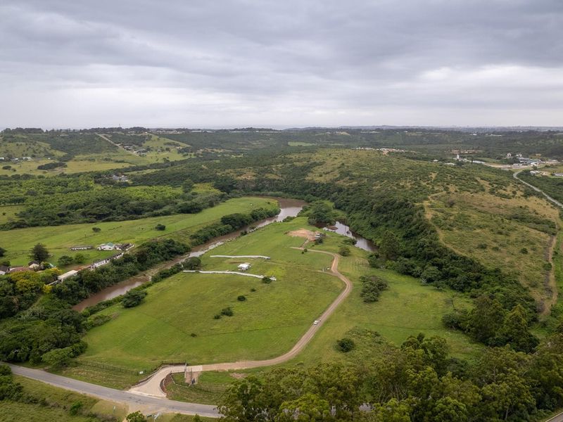 Aerial view of a large, vacant residential land parcel featuring rolling green hills, river frontage, and established gravel access road.