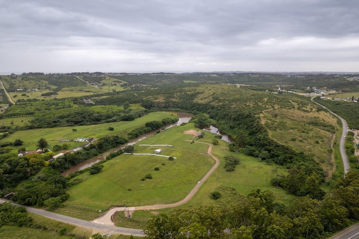 Aerial view of a large, vacant residential land parcel featuring rolling green hills, river frontage, and established gravel access road.