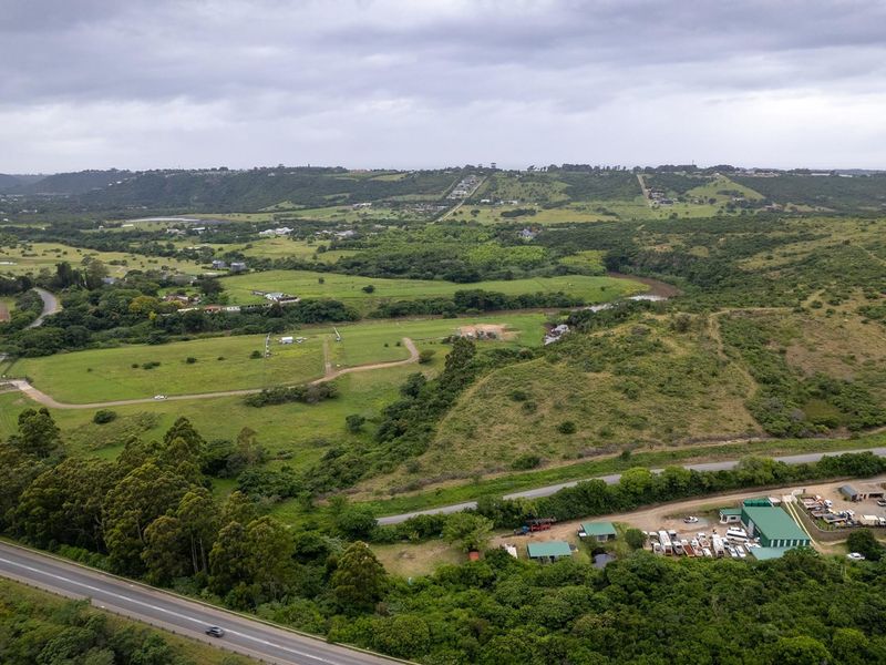 An aerial view of a large, undeveloped residential land parcel featuring rolling green hills, natural vegetation, and proximity to local road infrastructure.