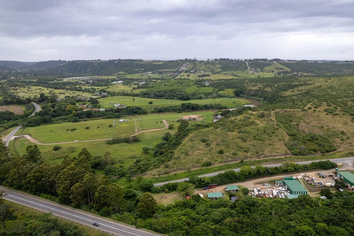 An aerial view of a large, undeveloped residential land parcel featuring rolling green hills, natural vegetation, and proximity to local road infrastructure.