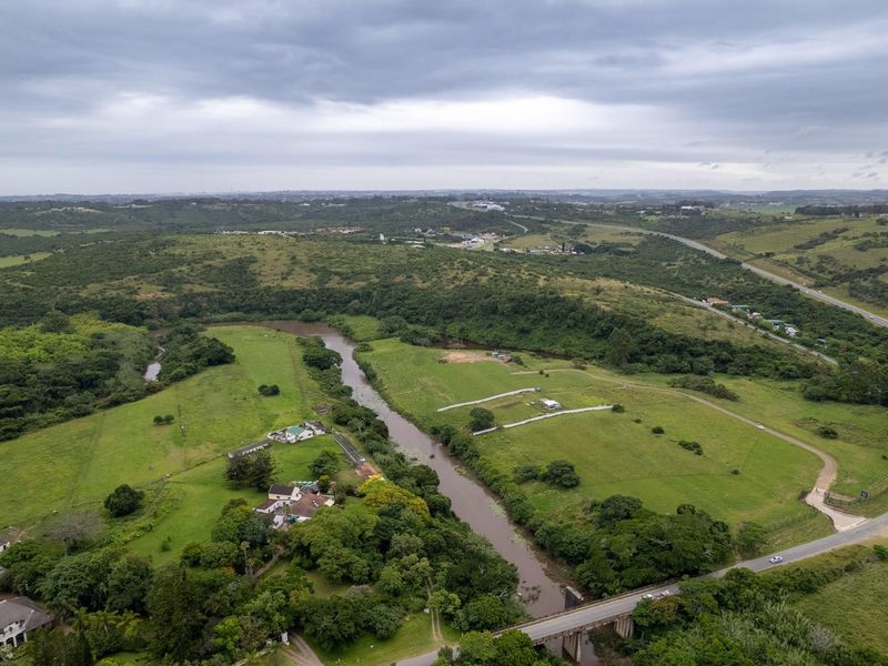 An aerial view of the residential land parcel featuring expansive green fields, a river running through the property, and surrounding road infrastructure.