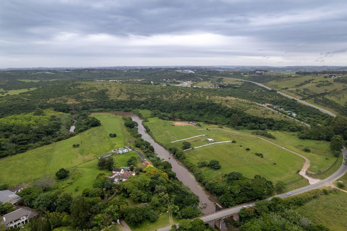 An aerial view of the residential land parcel featuring expansive green fields, a river running through the property, and surrounding road infrastructure.