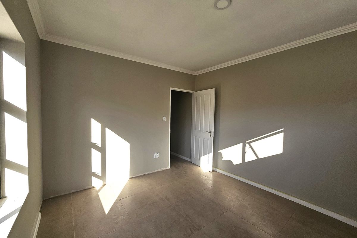 A bright, empty bedroom featuring neutral wall paint, tiled flooring, and crown molding, illuminated by natural light from the side window.