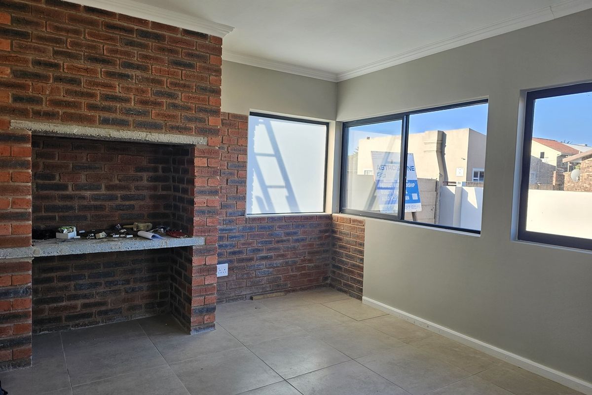 An indoor entertainment area featuring a built-in brick fireplace, tiled flooring, and large windows providing natural light.