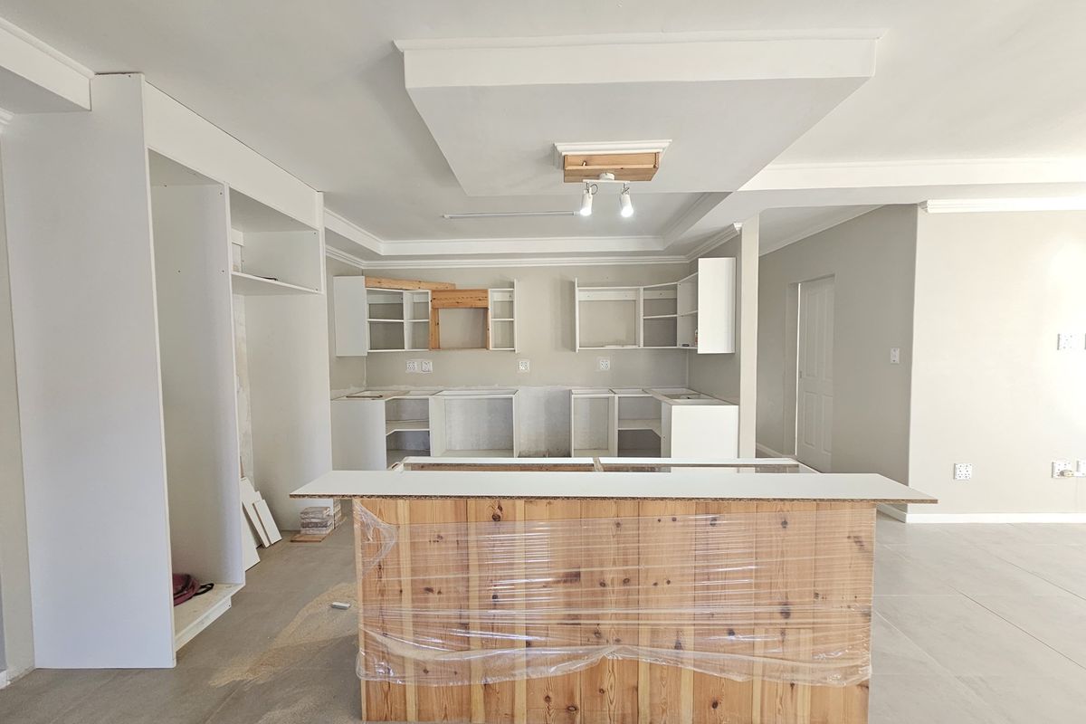 An unfinished kitchen space featuring a central island, base and wall cabinetry, and a recessed ceiling detail, currently undergoing renovation.