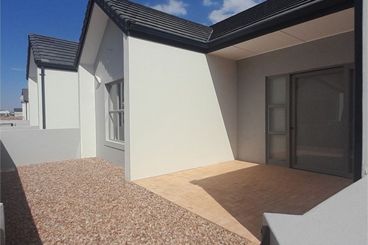 A clean rear exterior view of the townhouse featuring a paved patio area and a low-maintenance gravel garden space.