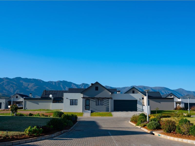 Front elevation of a modern residential property featuring a paved driveway, double garage, and well-maintained garden with scenic mountain views in the background.