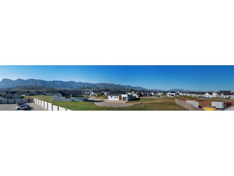A panoramic aerial view of a residential estate featuring modern homes, paved roads, and scenic mountain views in the background.