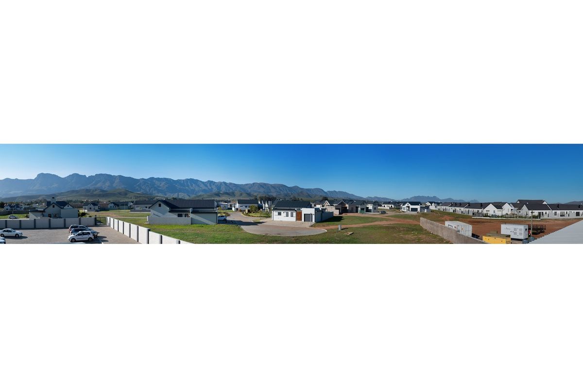 A panoramic aerial view of a residential estate featuring modern homes, paved roads, and scenic mountain views in the background.