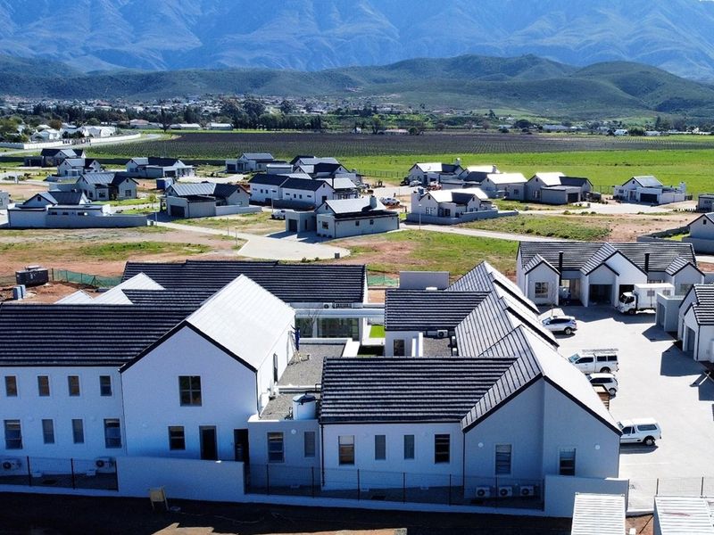 Aerial view of a modern residential estate featuring contemporary homes with tiled roofs, paved driveways, and scenic mountain views in the background.