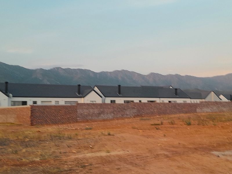 A scenic view of a residential development featuring a brick boundary wall with a backdrop of mountains.