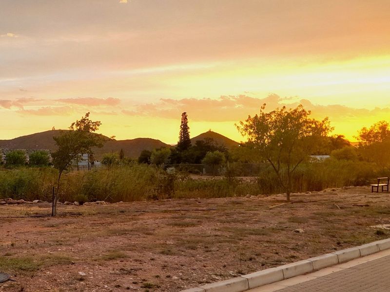 A scenic view of the vacant residential land at sunset, featuring natural landscape, distant hills, and a paved curb along the property edge.