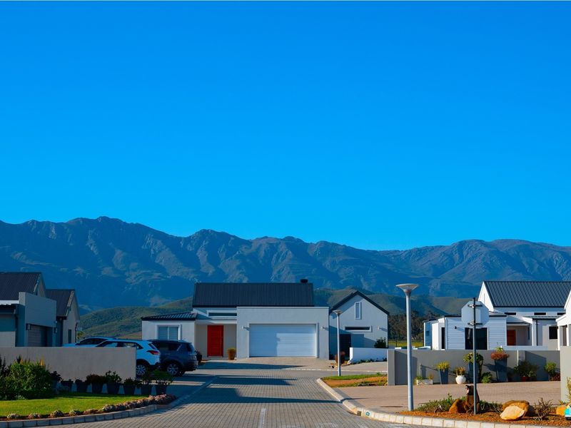 A clear street view of a modern residential estate featuring paved driveways, contemporary homes with metal roofs, and scenic mountain views in the background.
