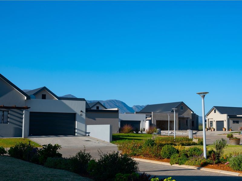 A clear street view of a modern residential estate featuring paved driveways, garages, and well-maintained landscaped gardens against a mountain backdrop.