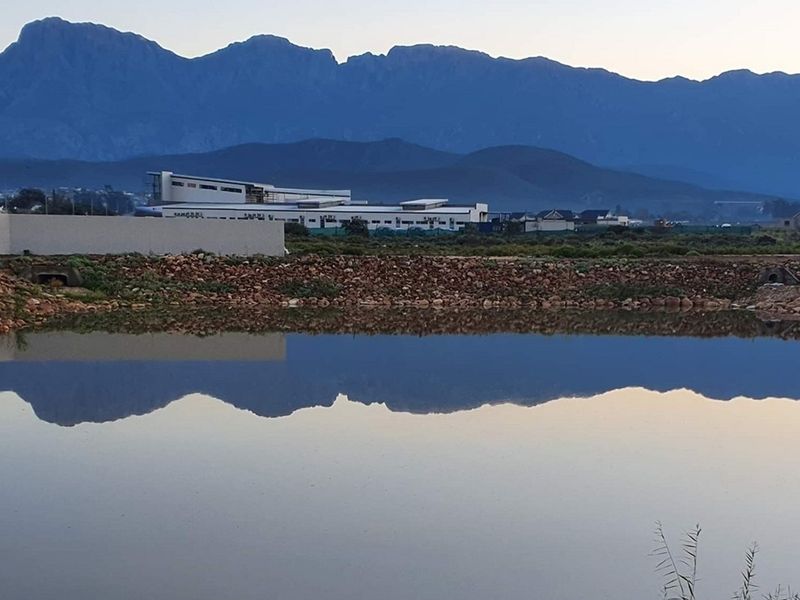 Scenic view of a tranquil pond reflecting the surrounding mountain range and nearby residential development.