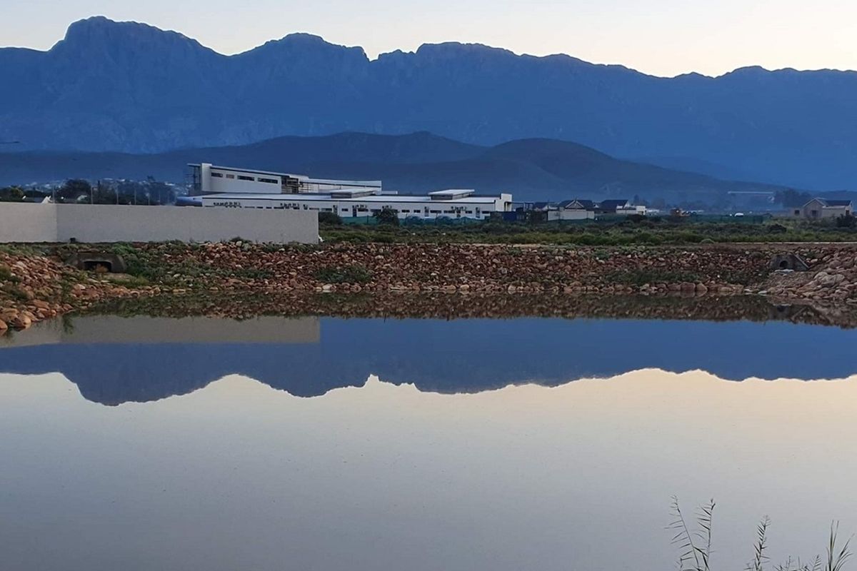 Scenic view of a tranquil pond reflecting the surrounding mountain range and nearby residential development.