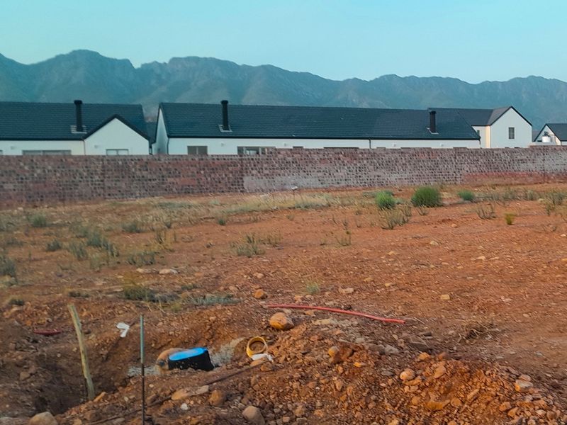 Vacant residential plot featuring a boundary wall, mountain views, and visible underground utility connections ready for development.
