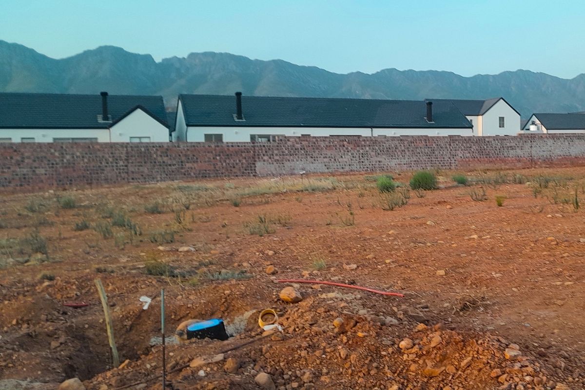 Vacant residential plot featuring a boundary wall, mountain views, and visible underground utility connections ready for development.