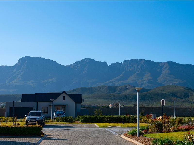 A scenic view of the residential property featuring a paved driveway, landscaped garden, and a stunning mountain backdrop.