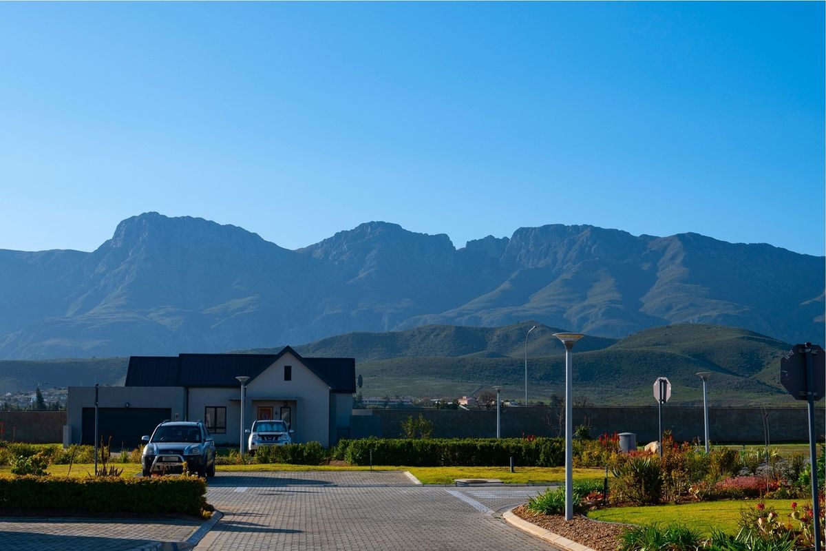 A scenic view of the residential property featuring a paved driveway, landscaped garden, and a stunning mountain backdrop.