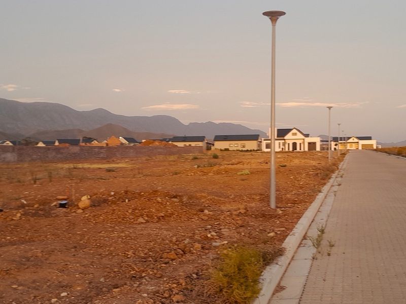 A view of a residential street in a developing estate, featuring paved roads, street lighting, and surrounding mountain views.