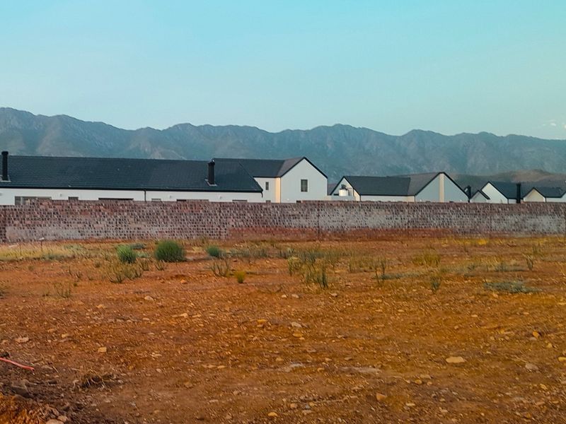 A vacant residential plot featuring a boundary wall with scenic mountain views in the background.