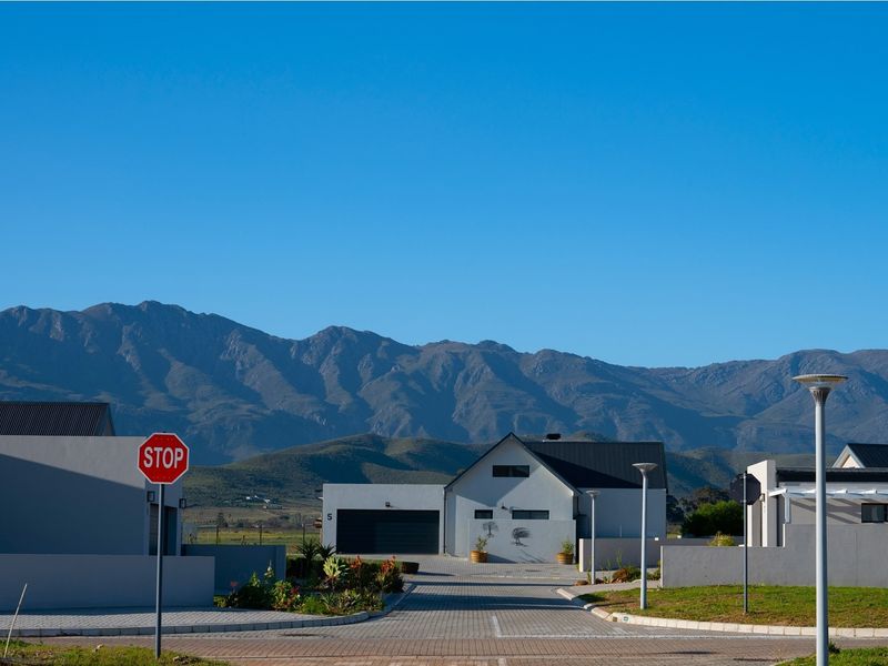 A clear street-level view of a modern residential property featuring a paved driveway, garage, and scenic mountain backdrop.