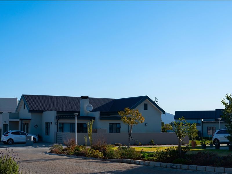 A view of the front exterior of a residential property featuring a paved driveway, landscaped garden, and a modern home with a metal roof.