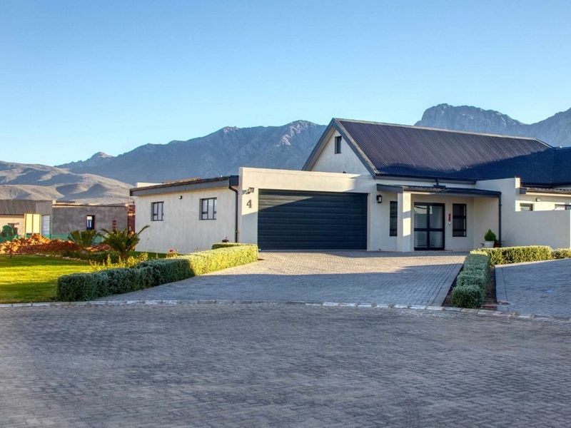 Front exterior view of a modern residential property featuring a paved driveway, double garage, and mountain backdrop.