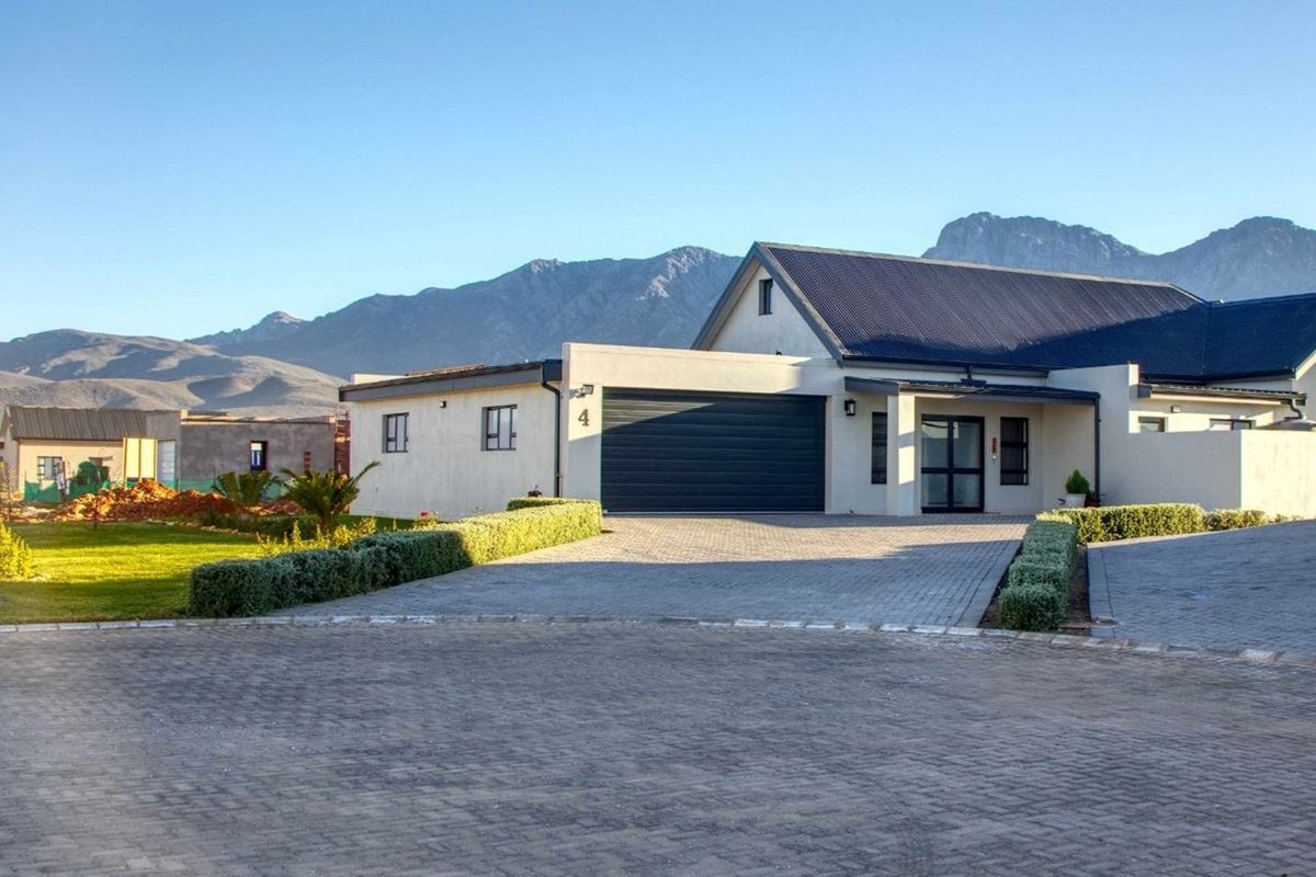 Front exterior view of a modern residential property featuring a paved driveway, double garage, and mountain backdrop.