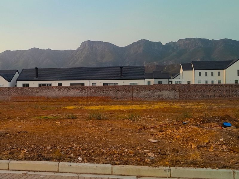A vacant residential plot featuring a brick boundary wall with scenic mountain views in the background.