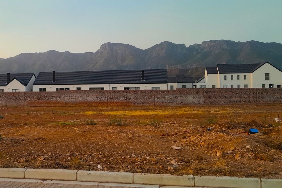 A vacant residential plot featuring a brick boundary wall with scenic mountain views in the background.