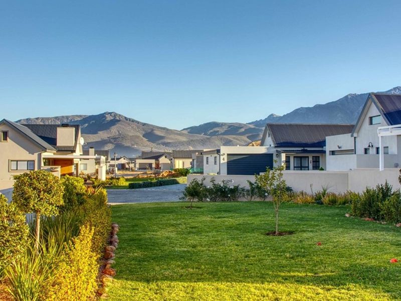 A scenic view of a well-maintained residential estate featuring landscaped gardens, paved driveways, and a backdrop of mountain ranges.