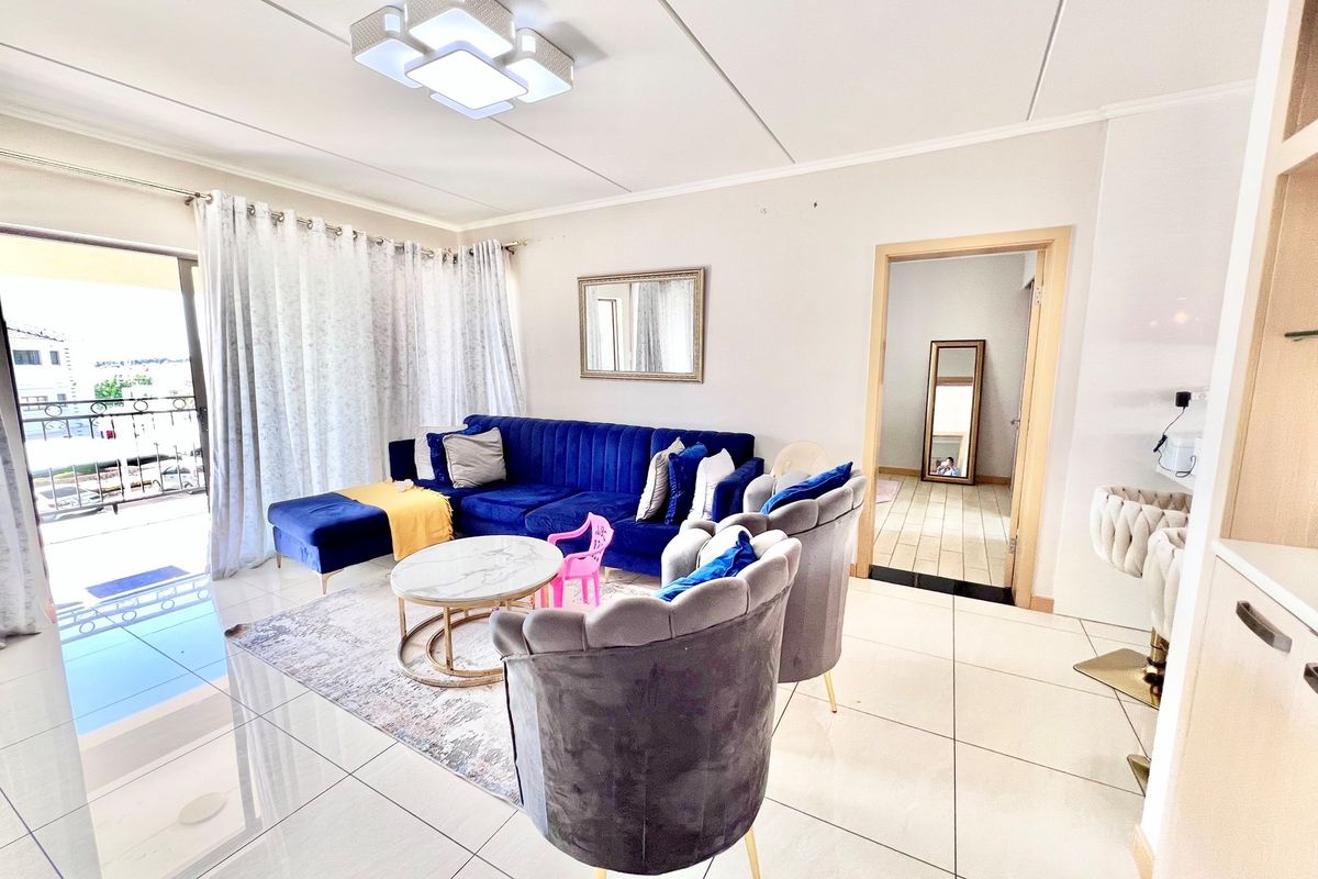 A bright and spacious living room featuring large floor tiles, a modern ceiling light fixture, and direct access to an outdoor balcony.