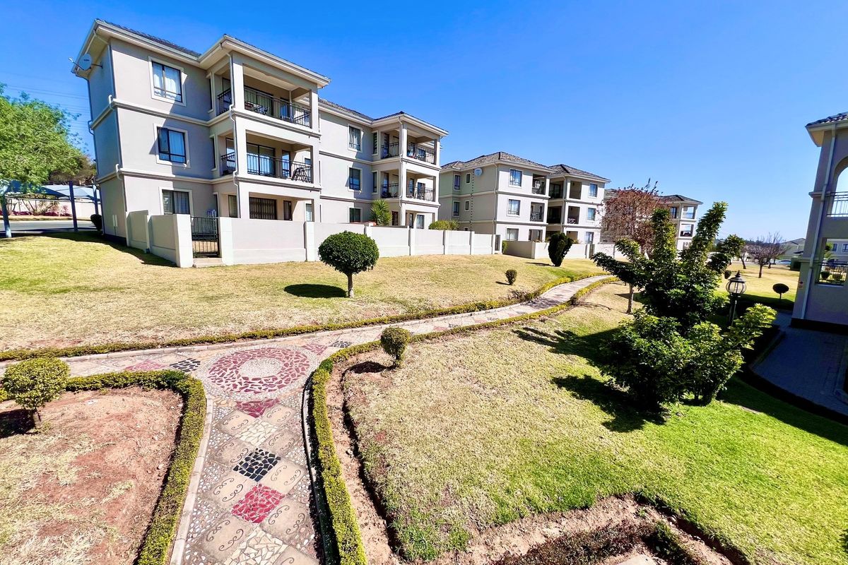 A view of the apartment complex exterior featuring landscaped gardens, paved walkways, and multi-story residential buildings with balconies.