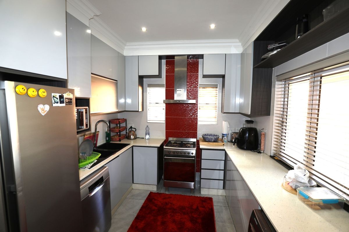 Modern kitchen featuring high-gloss cabinetry, stone countertops, a gas stove with extractor fan, and a striking red tiled splashback.