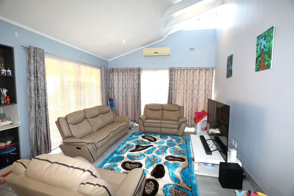 Spacious living room featuring a vaulted ceiling, split-system air conditioning, and large sliding glass doors providing ample natural light.