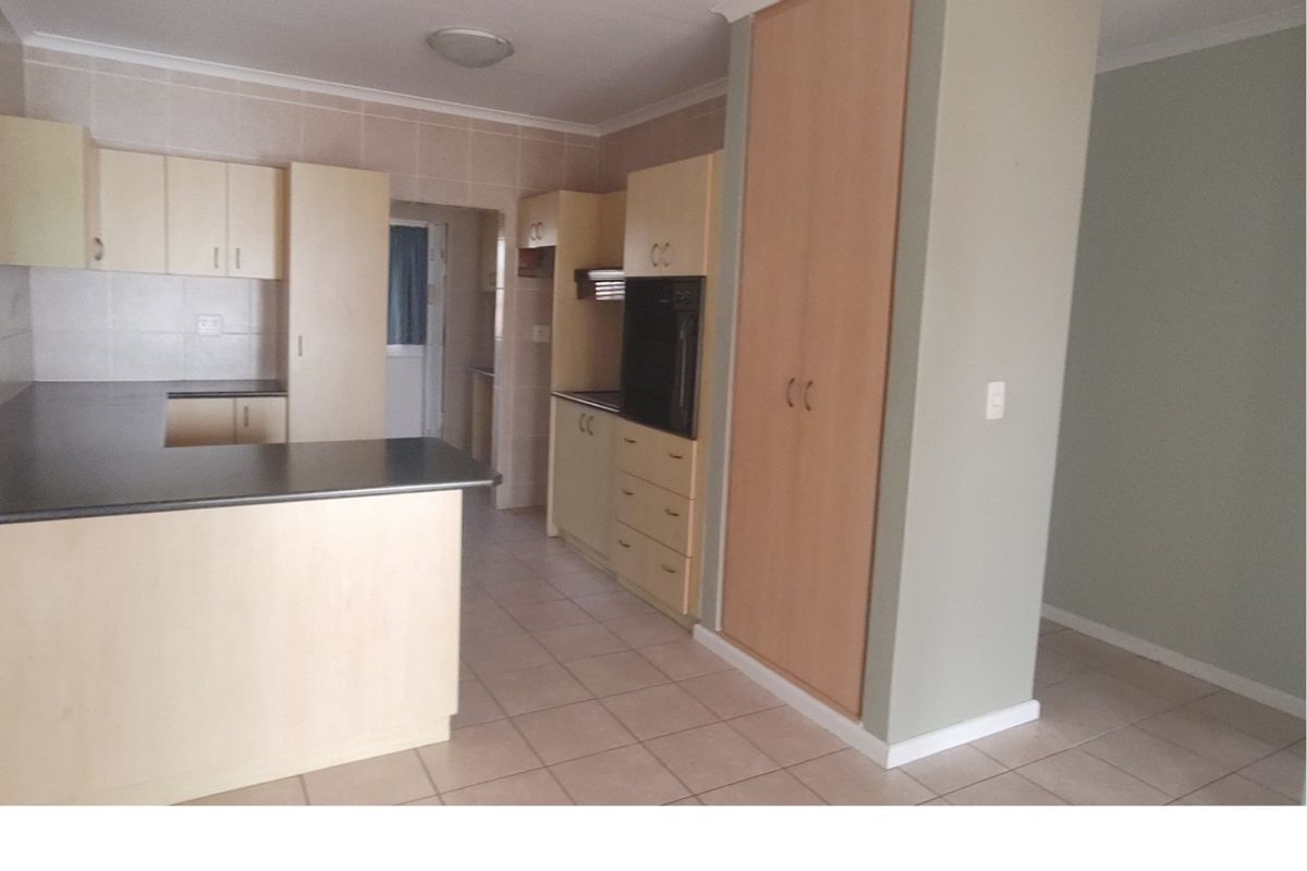 A functional kitchen featuring light wood cabinetry, dark countertops, built-in oven, and tiled flooring, offering a clean and practical layout.