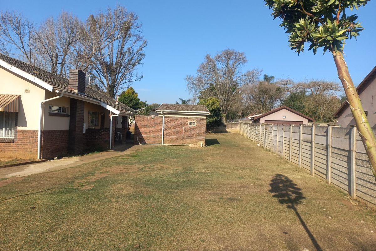 Spacious rear garden featuring a lawn, brick outbuilding, and precast concrete boundary wall, adjacent to the main house with a brick chimney.