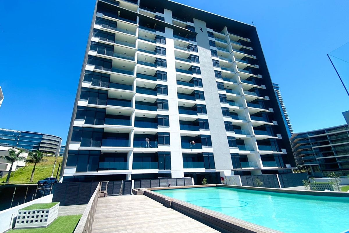 Modern multi-story apartment building exterior featuring glass balconies and a swimming pool with wooden decking.