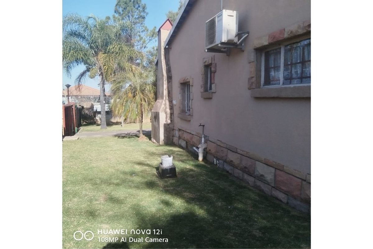 Rear exterior view of the house featuring stone cladding, an external air conditioning unit, and a chimney stack set against a lawn area.