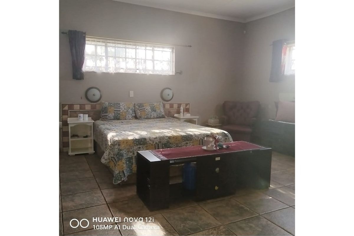 A spacious bedroom featuring tiled flooring, a built-in headboard, and windows fitted with security bars.