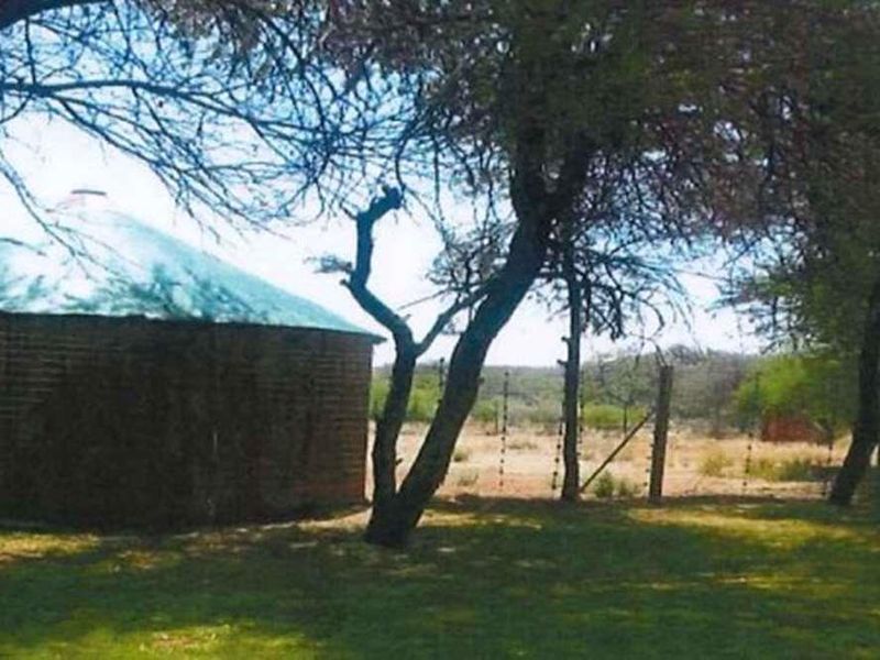 A view of a circular brick structure with a metal roof situated on a small holding, surrounded by mature trees and perimeter fencing.