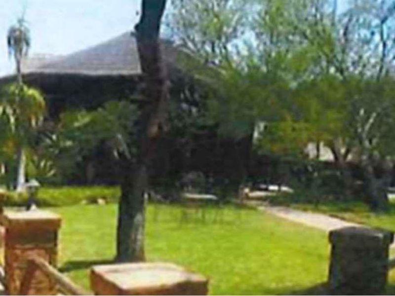 A view of the property grounds featuring a thatched roof structure, manicured lawn, and stone-accented boundary pillars.