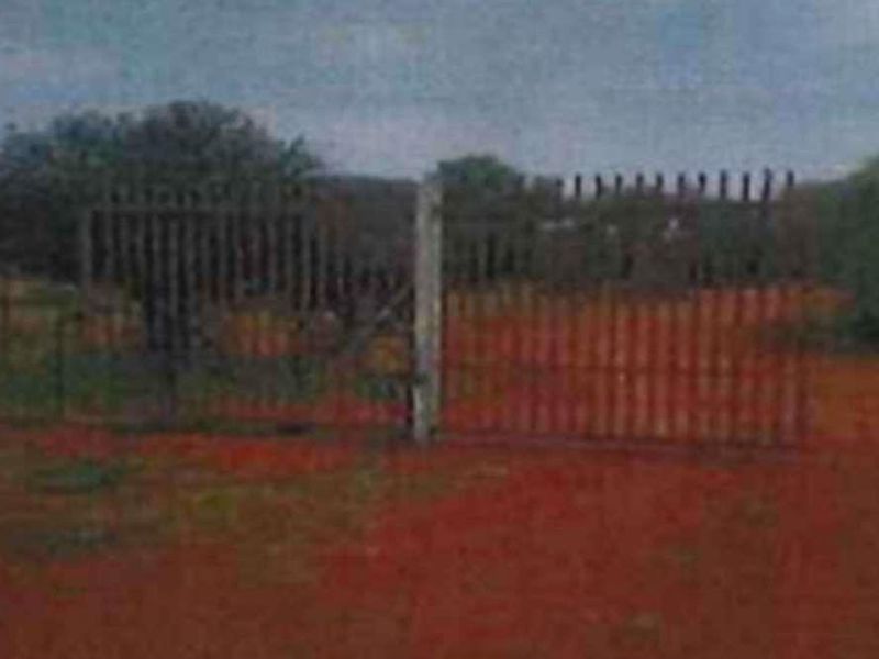 A view of the property entrance featuring a metal security gate and perimeter fencing on a rural small holding.