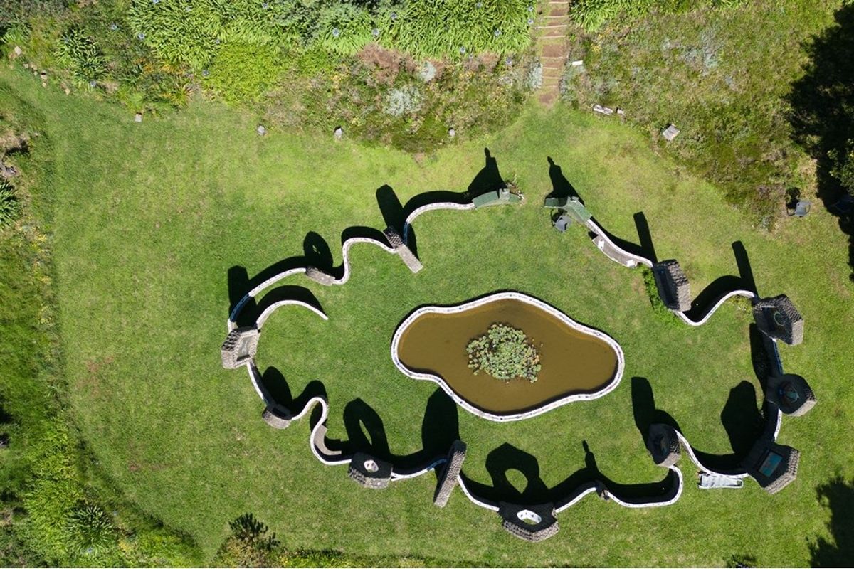 Aerial view of a landscaped garden featuring a central pond surrounded by a decorative, winding stone wall structure.