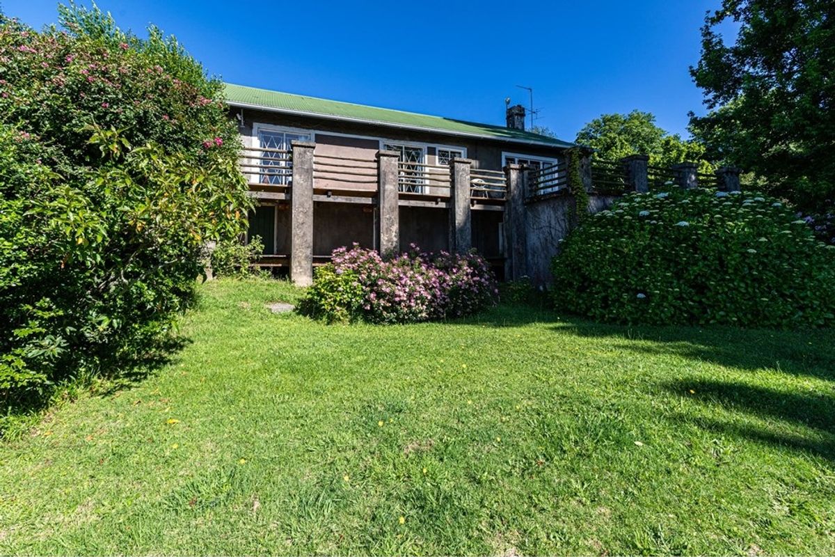 Rear view of the house featuring a raised wooden deck with stone pillars, overlooking a spacious garden area.