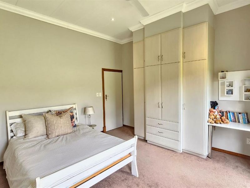 A well-maintained bedroom featuring neutral walls, carpeted flooring, built-in cupboards, and a ceiling fan.
