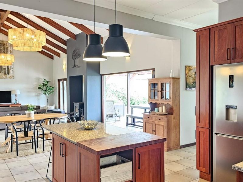 Spacious open-plan living area featuring a modern kitchen with timber cabinetry, granite island, vaulted ceilings with exposed beams, and a cozy fireplace.