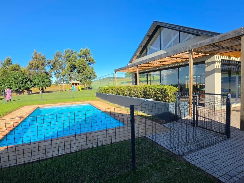 Outdoor pool area featuring a paved patio, timber pergola, and modern architectural design with large glass sliding doors overlooking the garden.